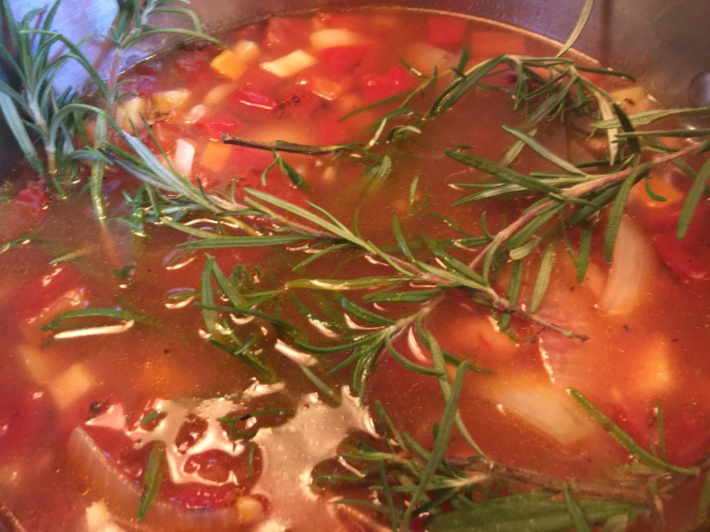 Pot of vegetable and bean soup with rosemary sprigs