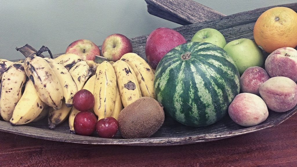 Bananas, plums, kiwi, apples, watermelon, peaches and grapefruit on a long wooden tray