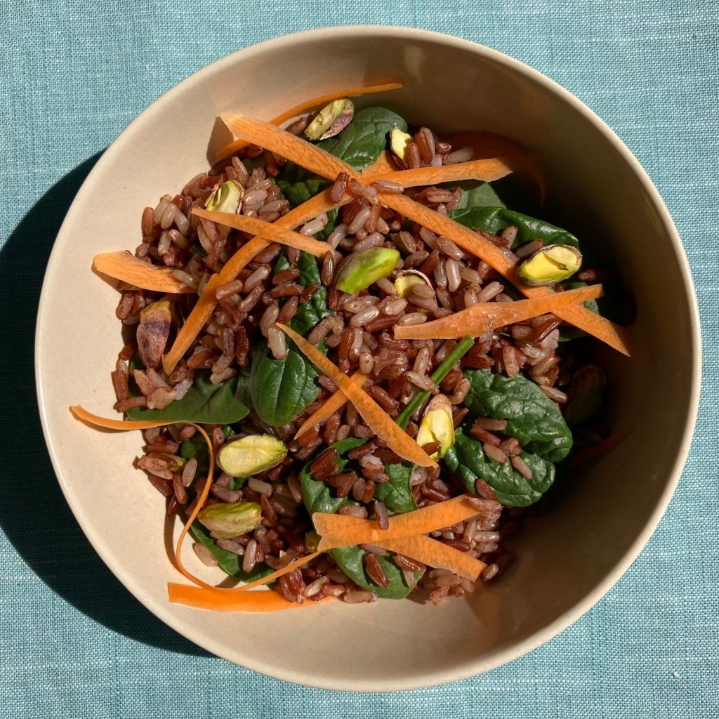 Bowl of red and brown rice with baby spinach, shredded carrots and pistachios