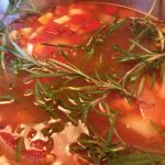 close up of vegetable bean soup in a pot with fresh rosemary sprig