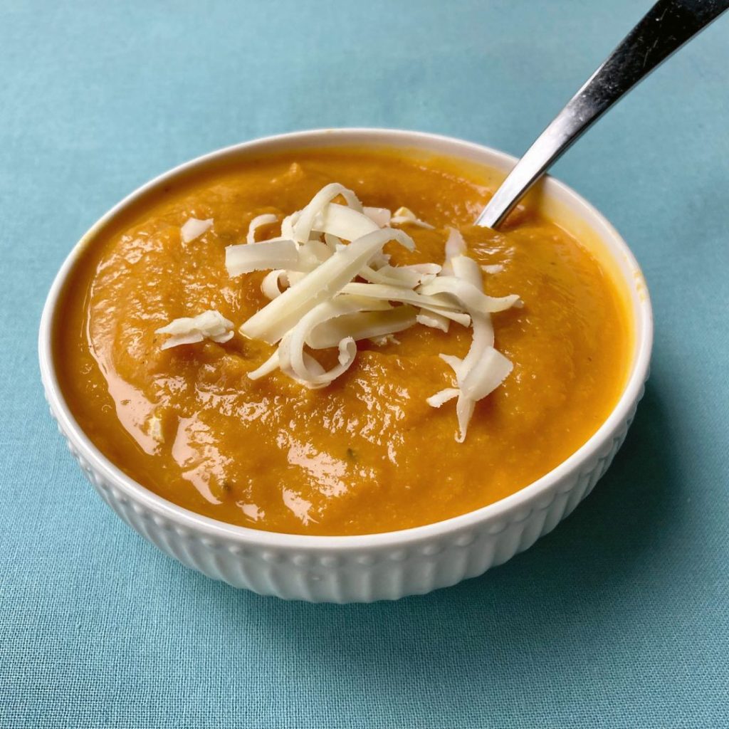 bowl of pumpkin chickpea soup and shredded cheese with a spoon