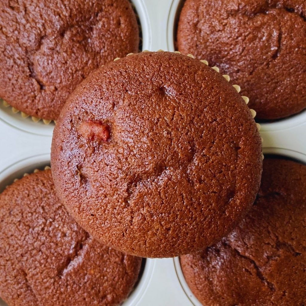 close-up of a chocolate strawberry muffin on a muffin pan filled with more chocolate strawberry muffins